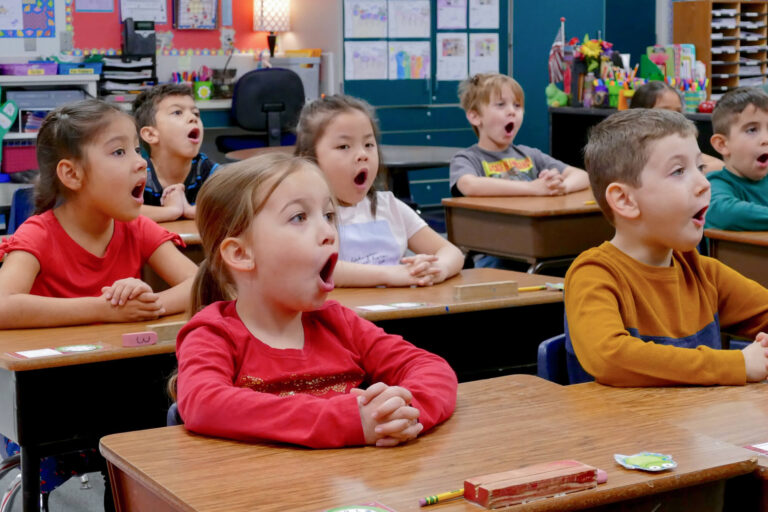 children seated at their desks sounding out words in class